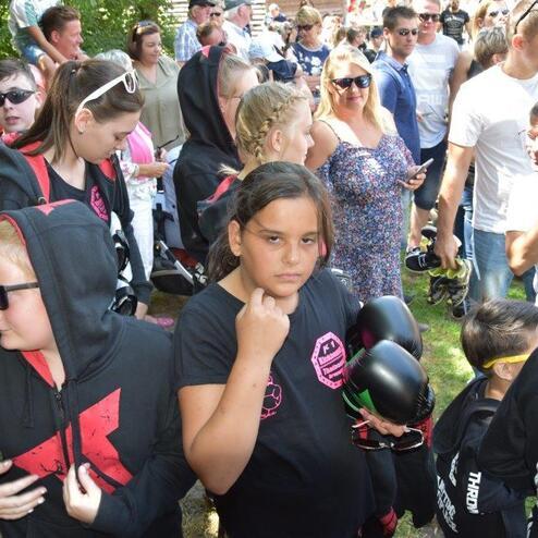 Gruppe von Jugendlichen in schwarzen Kapuzenpullis, einige tragen Sonnenbrillen, umgeben von einer Menschenmenge im Freien.