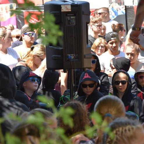 Wettkampfartige Veranstaltung mit zahlreichen Zuschauern; Gruppe in Kapuzenhoodies und Sonnenbrillen im Vordergrund.