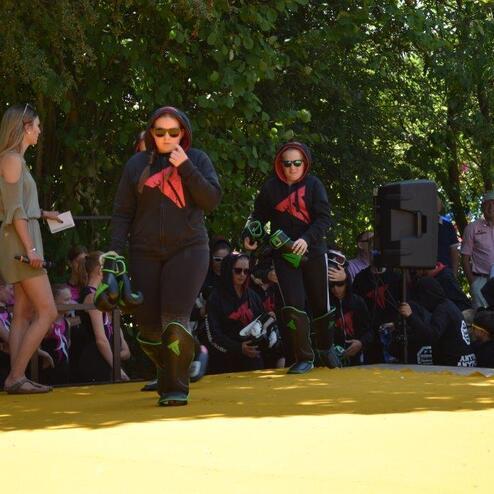 Zwei Frauen in schwarz-roten Outfits und Sonnenbrillen gehen &uuml;ber eine gelbe B&uuml;hne, Zuschauer im Hintergrund.