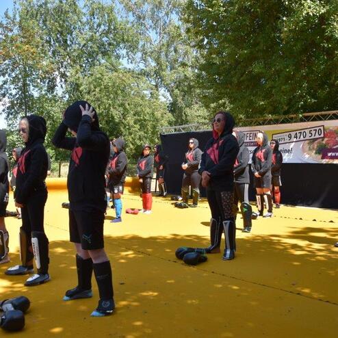 Gruppe von Kindern in schwarzen Trainingsanz&uuml;gen steht an einer gelben Fl&auml;che, bereit f&uuml;r ein Sportevent.