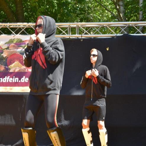 Zwei Personen in Sportkleidung mit Kapuzenpullovern stehen auf einer B&uuml;hne, im Hintergrund ein Werbebanner.