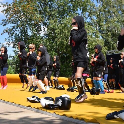 Gruppe von Kindern in Sportkleidung trainiert gemeinsam auf einer gelben Trainingsfl&auml;che im Freien.