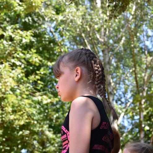 M&auml;dchen mit geflochtenem Haar steht im Freien vor B&auml;umen und schaut nachdenklich in die Ferne.