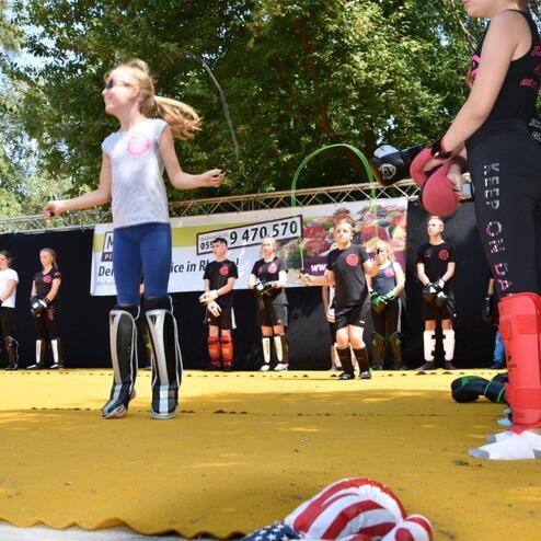 M&auml;dchen springt mit einem Seil auf einer gelben Matte, umgeben von weiteren Kindern in Sportkleidung.