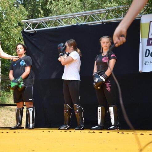 Vier M&auml;dchen in Sportkleidung mit Boxhandschuhen stehen auf einer Trainingsfl&auml;che. Fokus auf Bewegung und Vorbereitung.