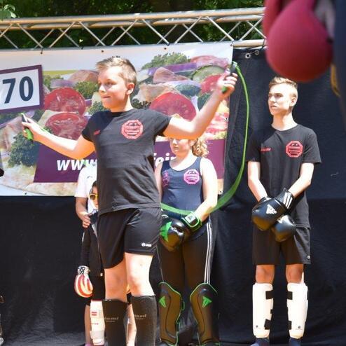 Kinder in Boxausr&uuml;stung stehen auf der B&uuml;hne, w&auml;hrend ein M&auml;dchen mit einem Springseil trainiert.