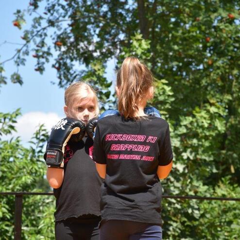 Zwei M&auml;dchen in Sportkleidung mit Boxhandschuhen trainieren im Freien auf einer Trainingsfl&auml;che.