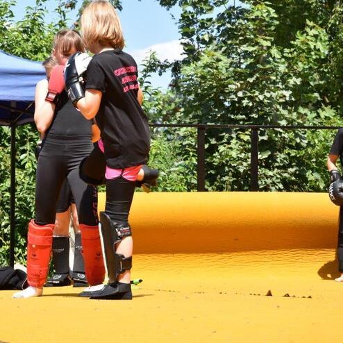 Vier Kinder im Training stehen auf einer gelben Matte, zwei davon tragen Schutzausr&uuml;stung und Boxhandschuhe.