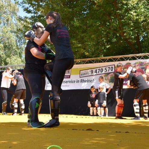 Zwei Frauen &uuml;ben Nahkampf-Techniken auf einer gelben Trainingsfl&auml;che w&auml;hrend eines Kampftrainings.