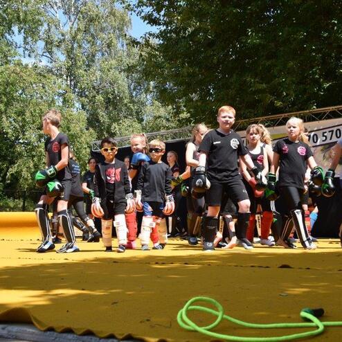 Gruppe von Kindern in Sportkleidung mit Boxhandschuhen auf einer gelben Matte bei einem Wettkampf.