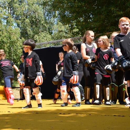 Gruppierung von Kindern in Sportbekleidung und Schutzausr&uuml;stung auf einer gelben Trainingsfl&auml;che beim Kampfsport-Training.