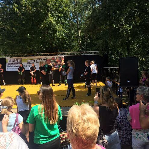 Menschenmenge bei einer Veranstaltung in einem Park, Blick auf einen Redner und eine Gruppe von Sportlern.