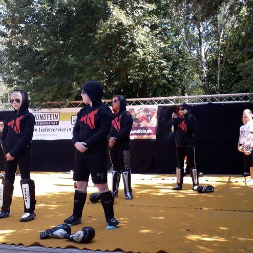 Gruppe von Jugendlichen in Sportanz&uuml;gen steht auf einer Matte, Vorbereitung auf einen Kampfsportauftritt im Freien.