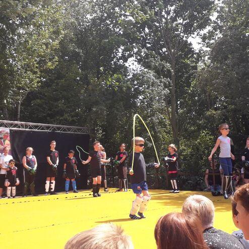 Kinder springen Seil auf einer B&uuml;hne w&auml;hrend einer Sportveranstaltung; Zuschauer sitzen im Vordergrund.