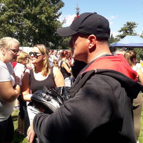 Ein Mann mit Boxhandschuhen steht in einer Menschenmenge, umgeben von Frauen, bei sonnigem Wetter im Freien.