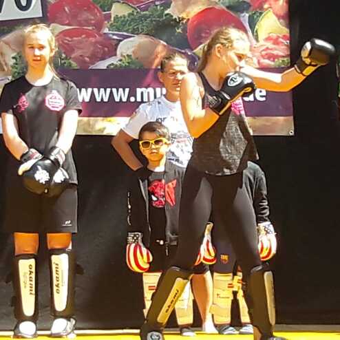 Gruppen&uuml;bung im Kampfsport mit Jugendlichen in Schutzausr&uuml;stung, die verschiedene Techniken demonstrieren.