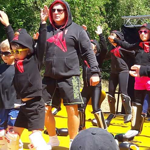 Gruppe von Menschen in Schwarz mit Kapuzenpullovern und Sonnenbrillen, die im Einklang auf einer gelben Fl&auml;che tanzen.