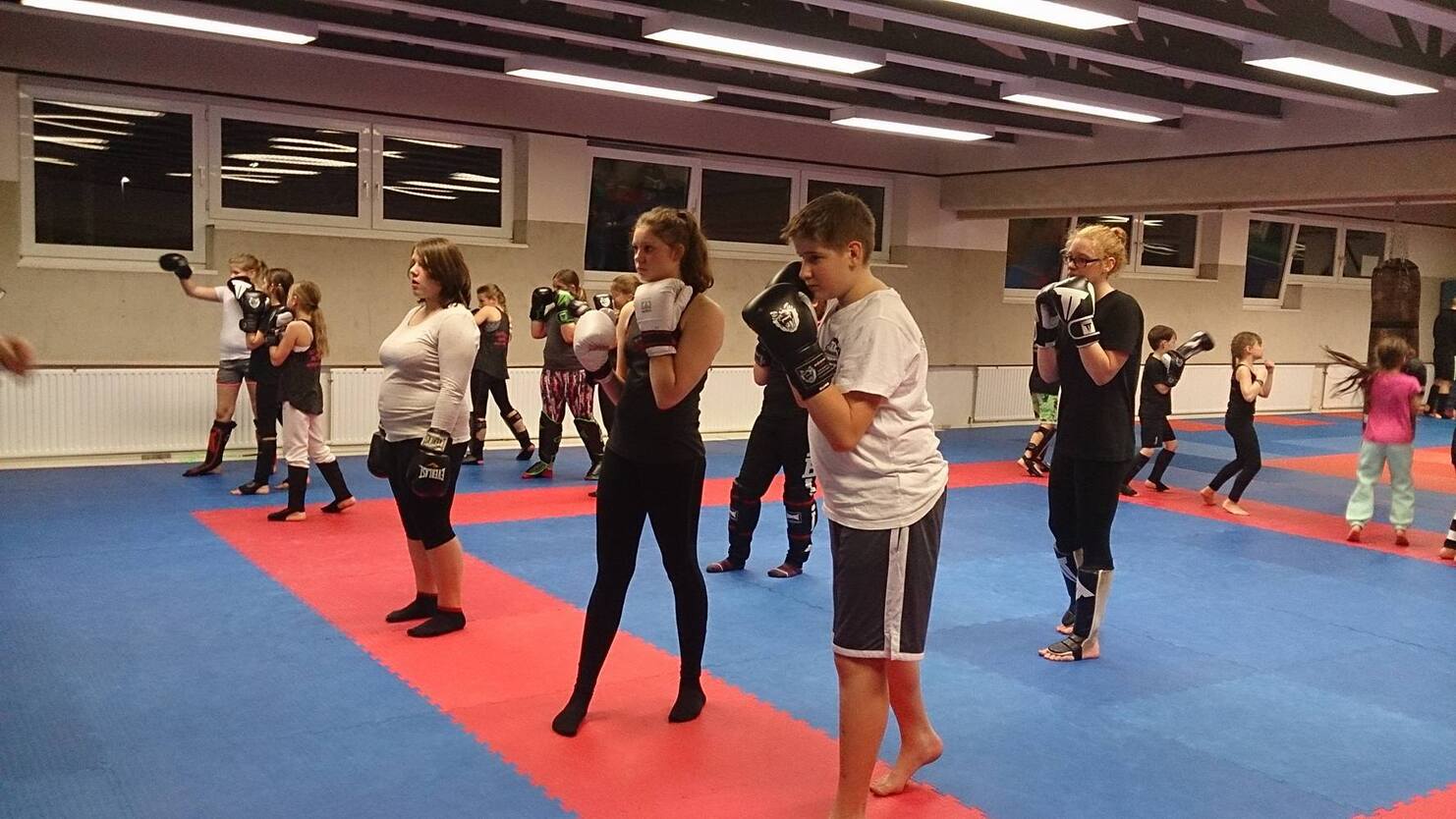 Gruppe von Trainierenden in Boxhandschuhen &uuml;bt in einem Raum auf einem blauen und roten Mattenboden.