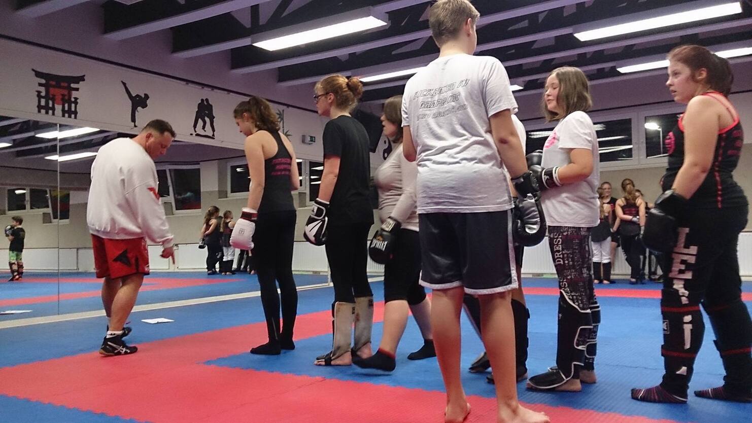 Gruppentraining im Kampfsport mit Trainer und Teilnehmern in Boxhandschuhen auf blauen und roten Matten.