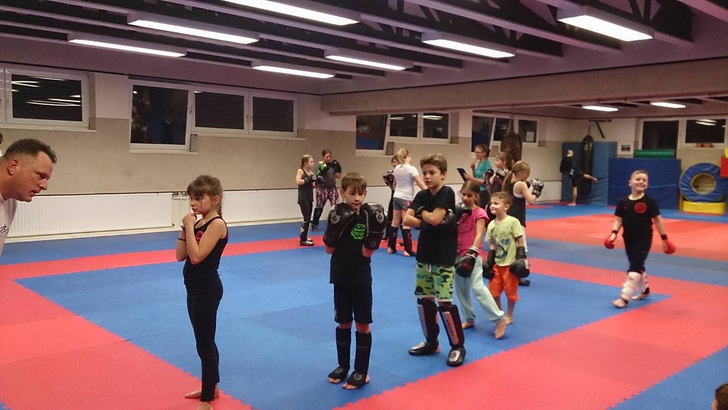 Gruppe von Kindern in Trainingskleidung &uuml;bt unter Anleitung eines Trainers in einem Kampfsportstudio.