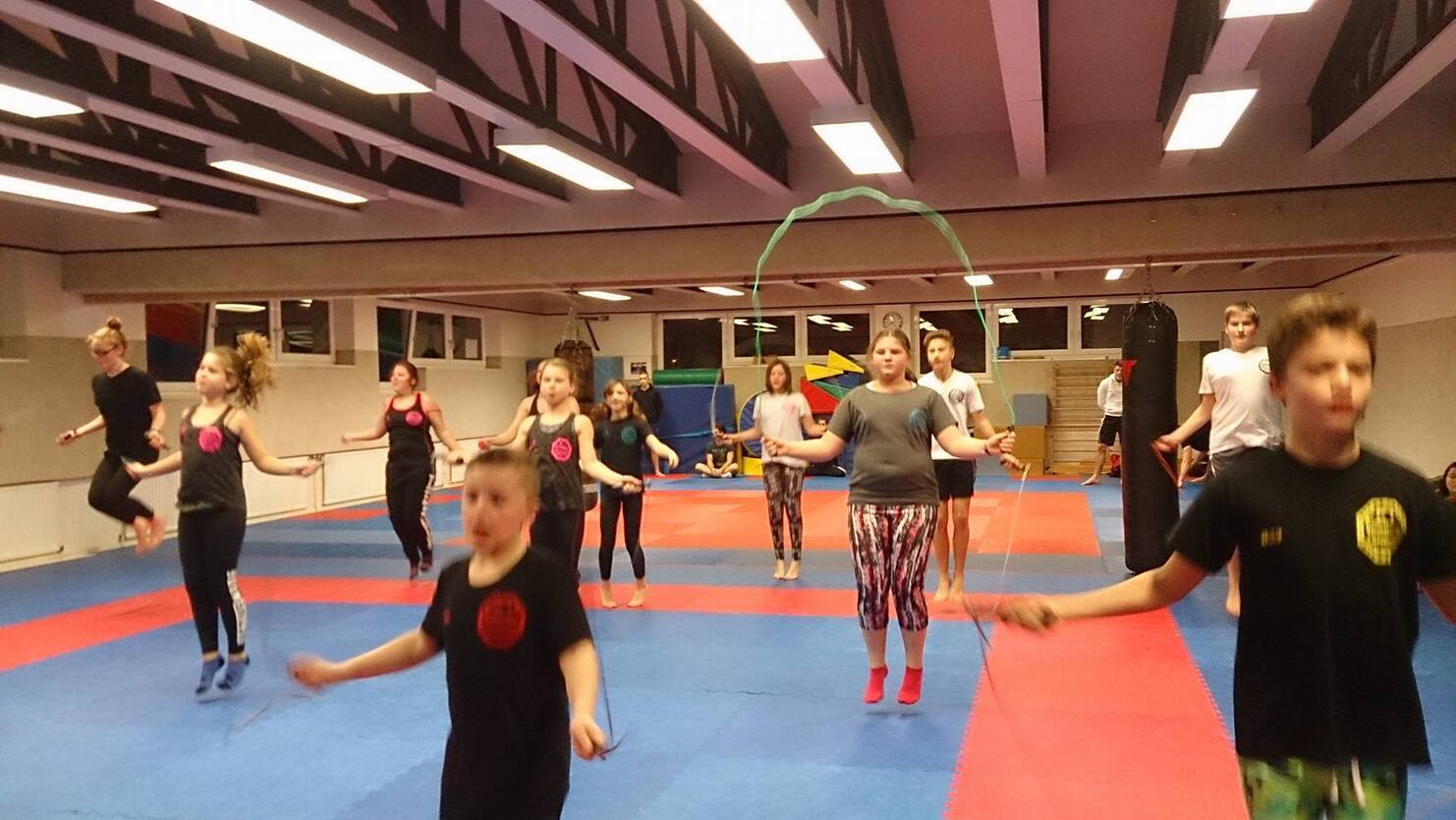 Gruppe von Jugendlichen springt mit Seilen in einem Trainingsraum mit blauer und roter Matte.