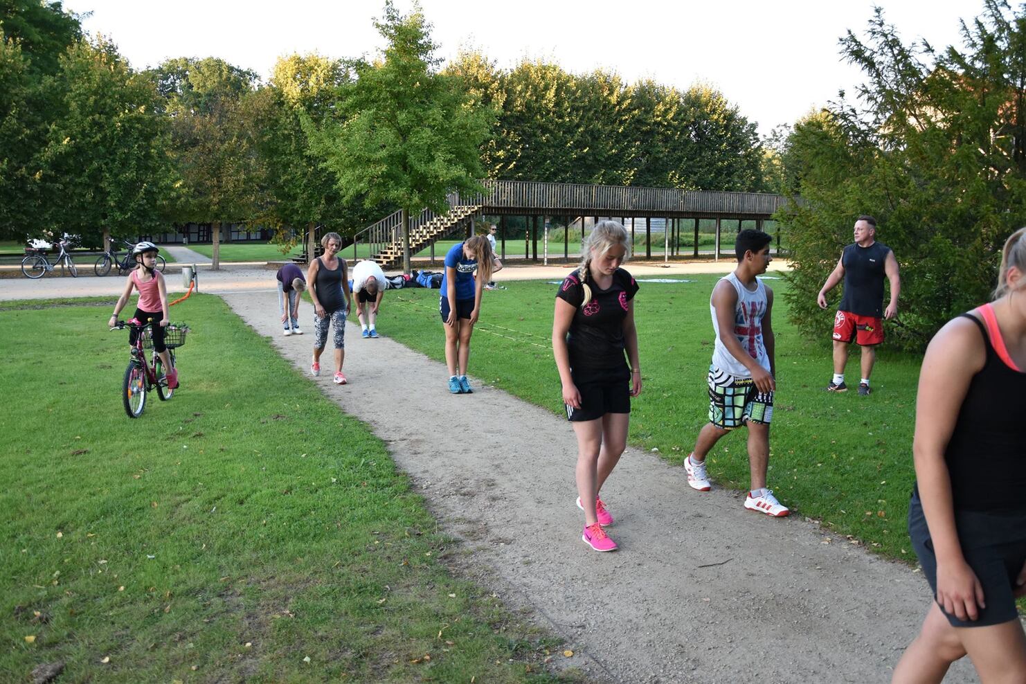 Gruppe von Menschen und einem Kind auf einem Fahrrad, die auf einem Weg im Park in Richtung Kamera gehen.