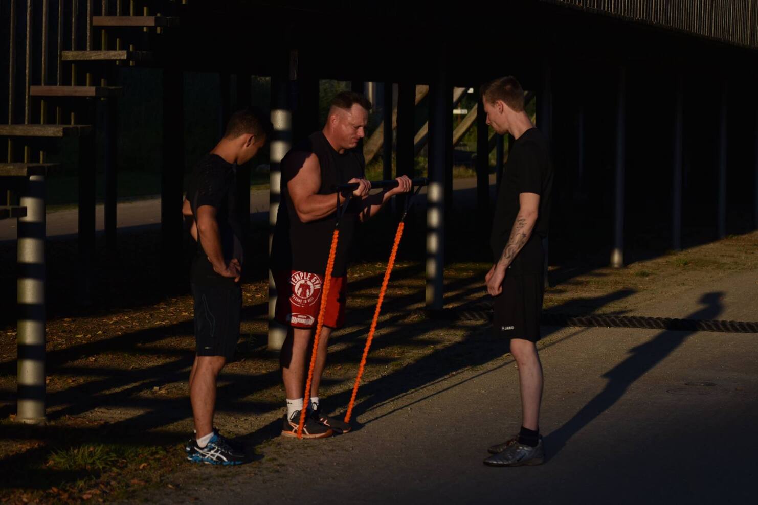 Drei M&auml;nner stehen im Freien und beobachten einen Mann, der ein Trainingsger&auml;t in der Hand h&auml;lt.