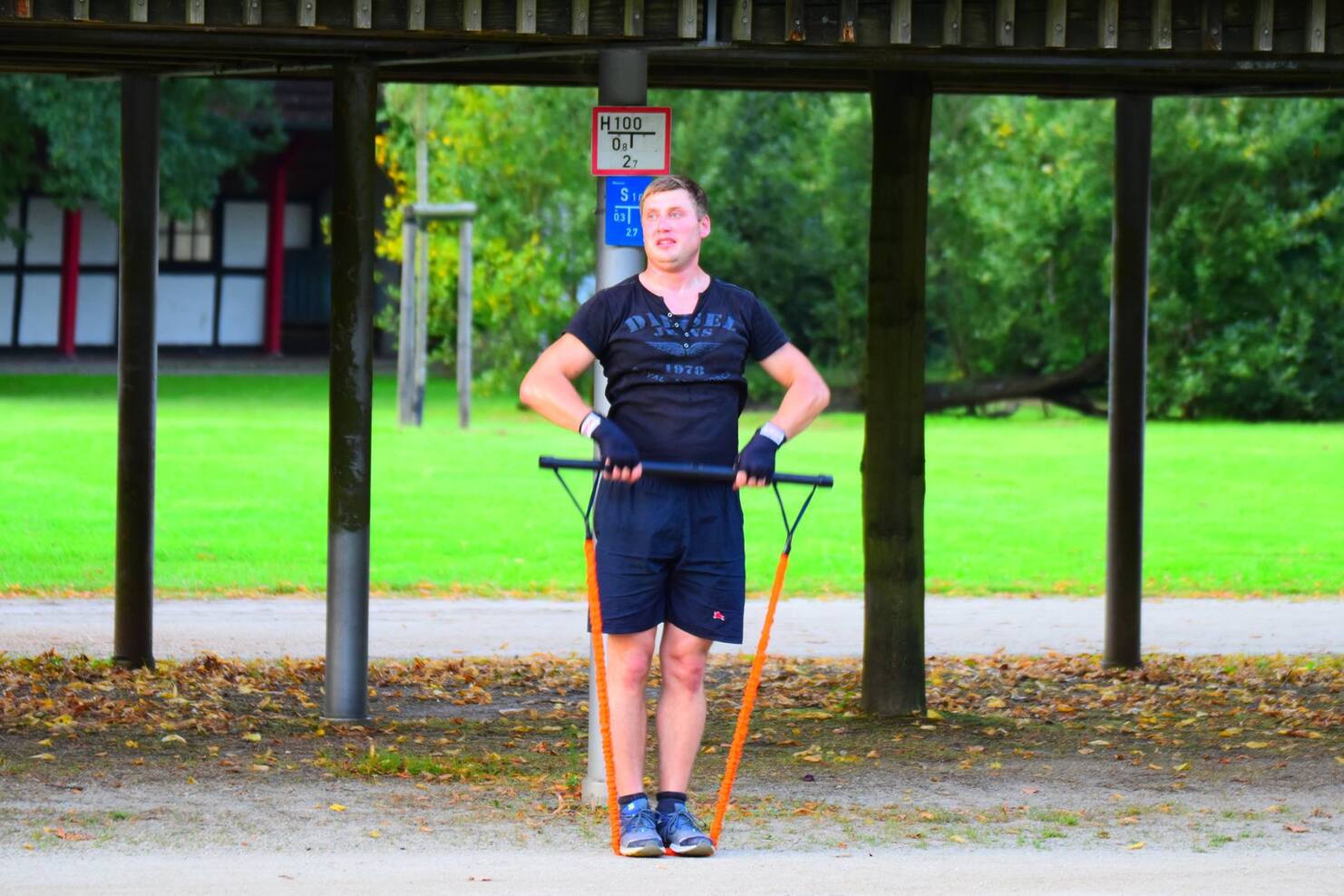 Mann in Sportkleidung trainiert mit Widerstandsb&auml;ndern unter einem &uuml;berdachten Bereich im Freien.