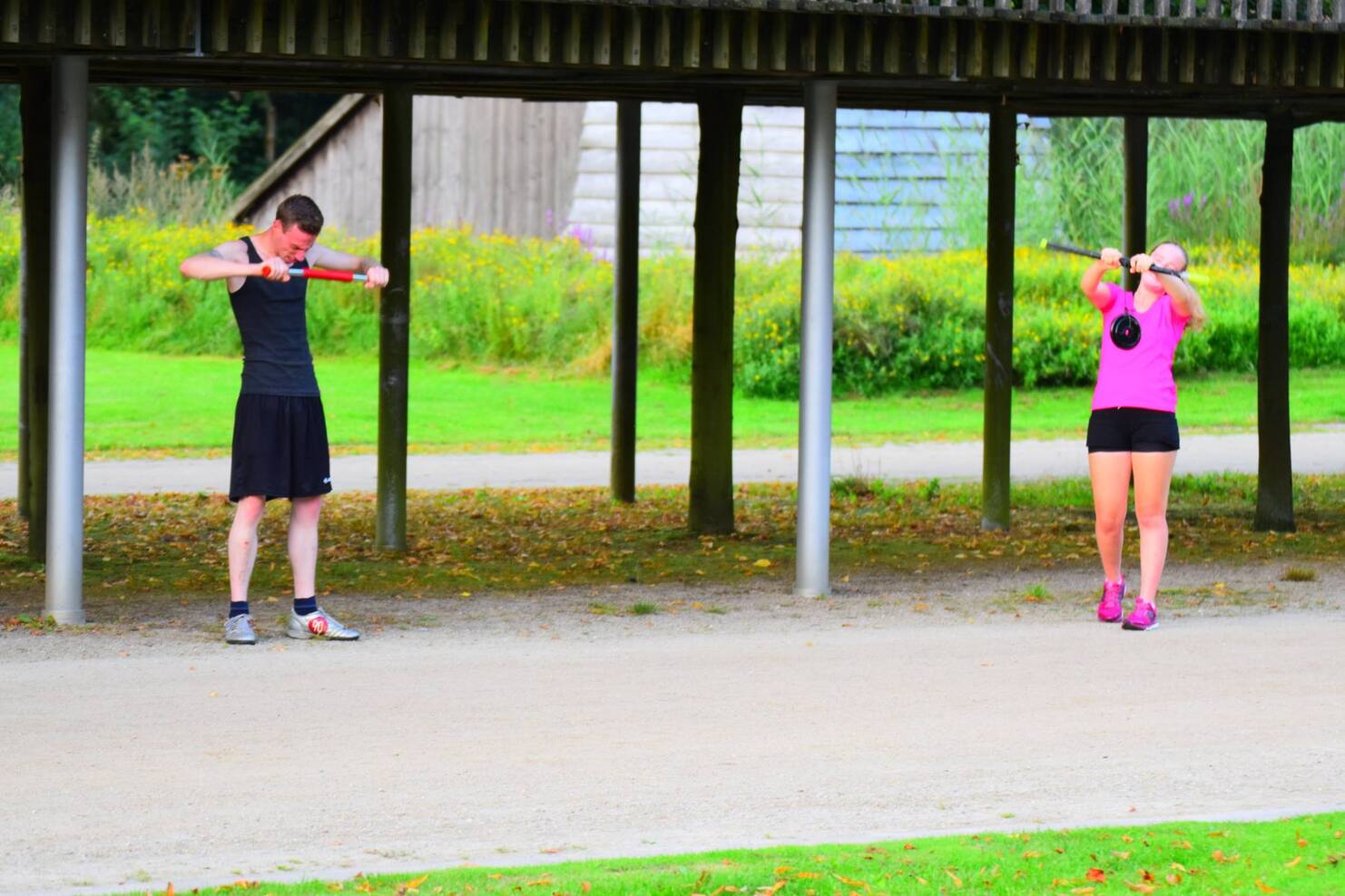 Zwei Personen trainieren unter einem &uuml;berdachten Bereich im Freien, beide halten Gewichte in ihren H&auml;nden.