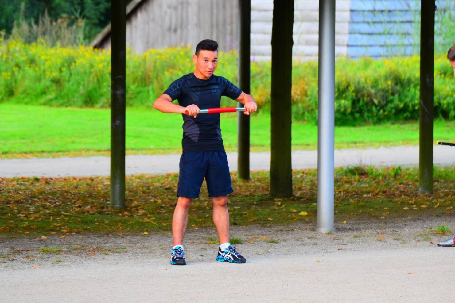 Mann in Sportkleidung f&uuml;hrt mit einem roten Trainingsstab &Uuml;bungen auf einem Freiluftplatz durch.