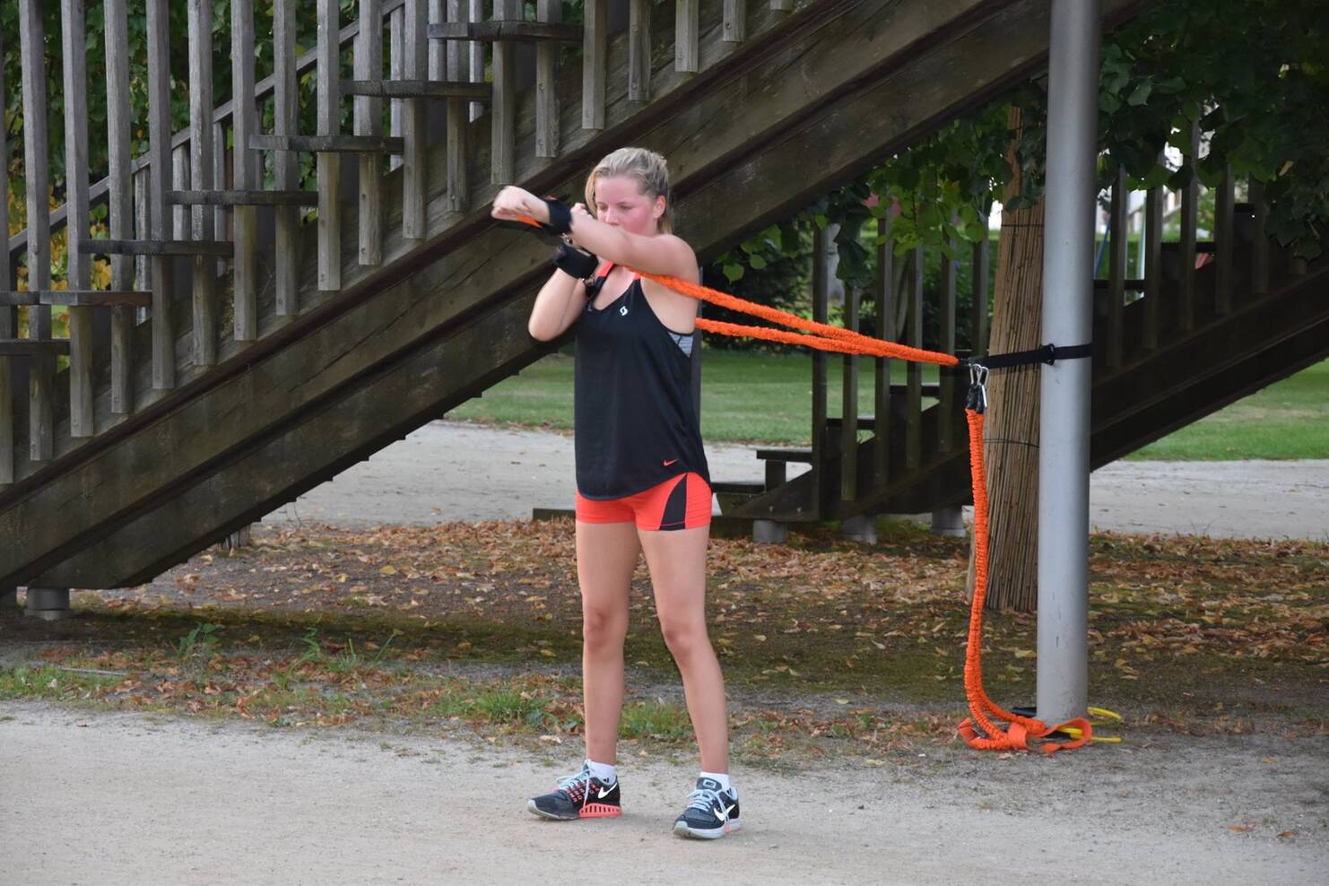Frau in Sportkleidung nutzt ein Widerstandsband, das an einem Pfosten befestigt ist, f&uuml;r ihr Training im Freien.