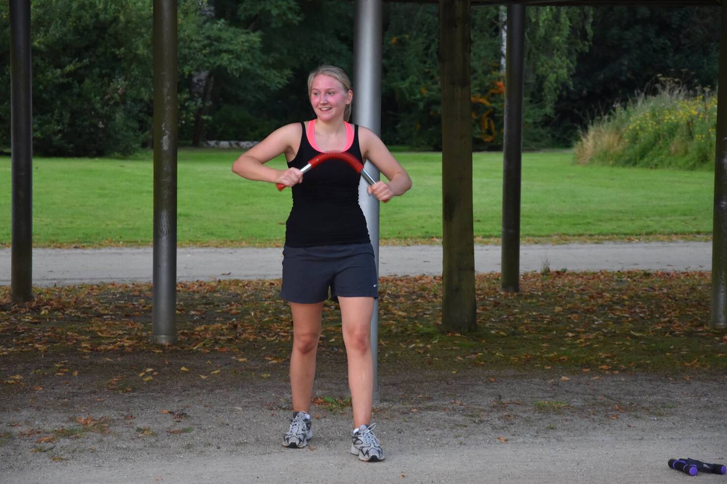 Frau in Sportkleidung mit einem roten Seil in der Hand, trainiert unter einer &Uuml;berdachung im Park.