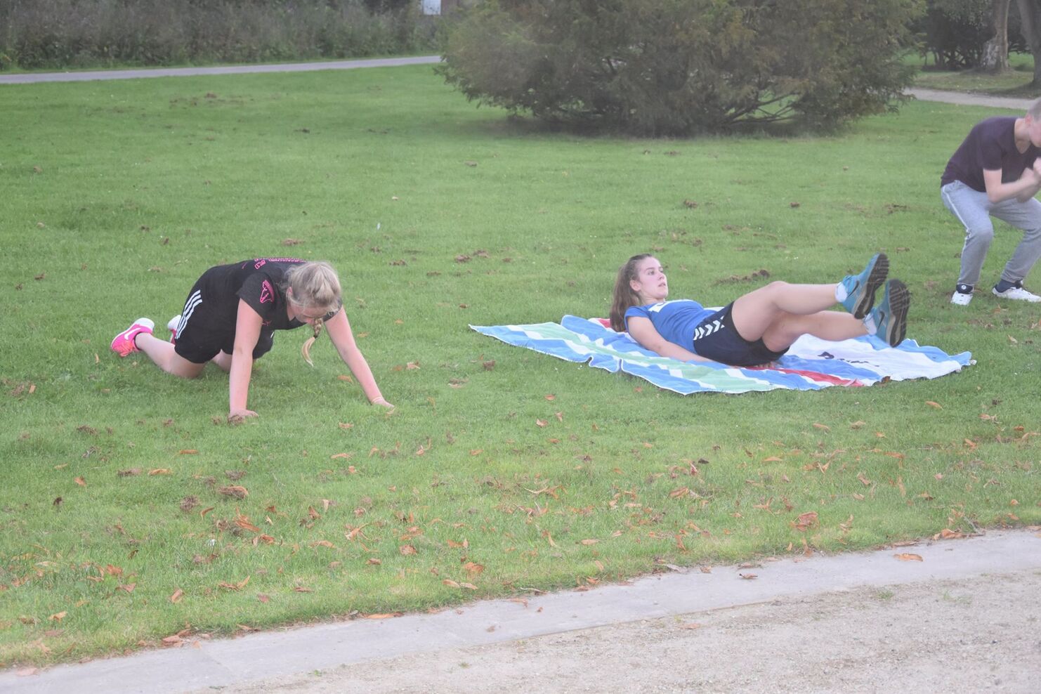 Zwei Frauen trainieren im Freien: eine macht Plank-&Uuml;bung, die andere hebt die Beine auf einem Handtuch.