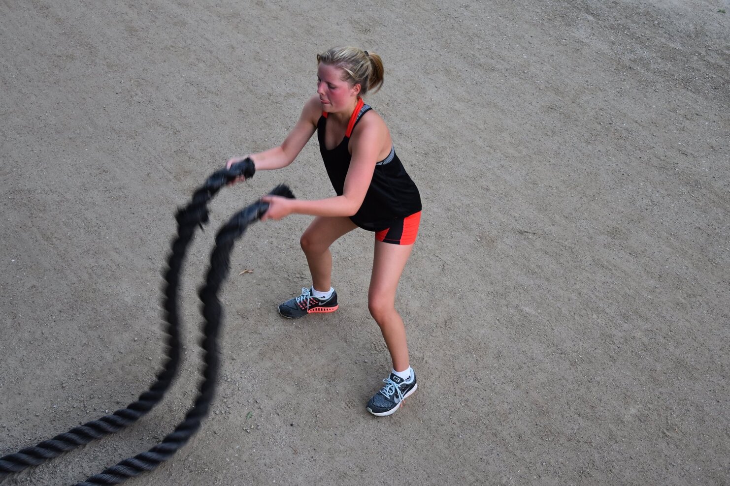 Frau mit Zopf trainiert mit schweren Seilen auf einem sandigen Untergrund.