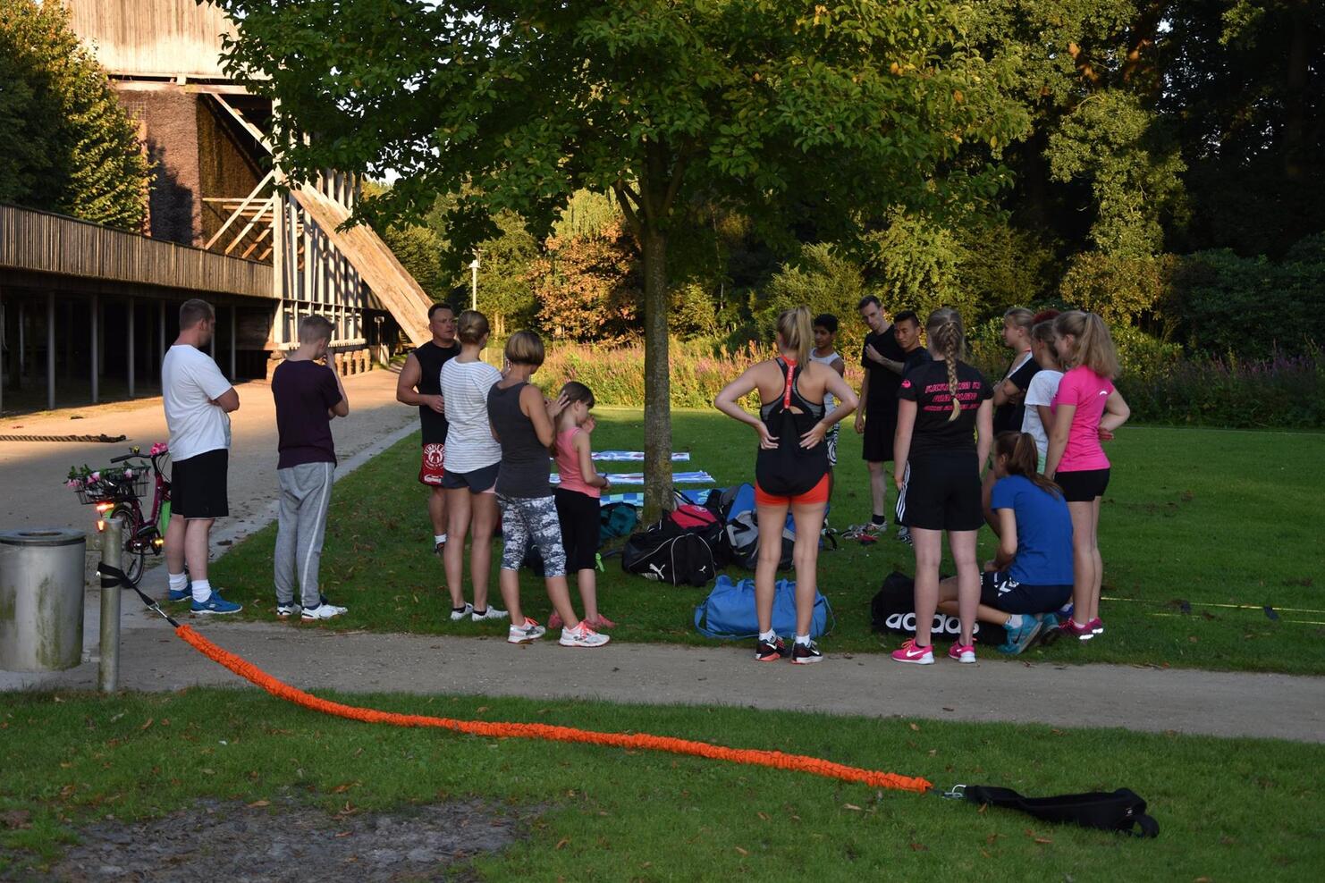 Gruppe von Sportlern in Sportbekleidung versammelt sich im Freien, um Anweisungen von einem Trainer zu erhalten.