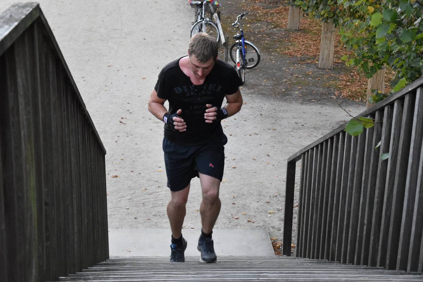 Mann in Sportkleidung l&auml;uft eine Treppe hoch, im Hintergrund stehen Fahrr&auml;der auf einem Weg zwischen B&auml;umen.