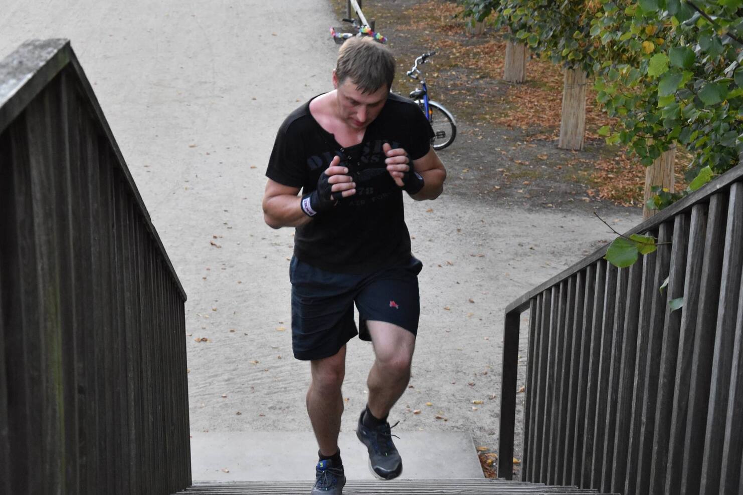 Mann mit Handschuhen joggt die Treppe hoch, im Hintergrund ein Fahrrad und herbstliche Pflanzen.