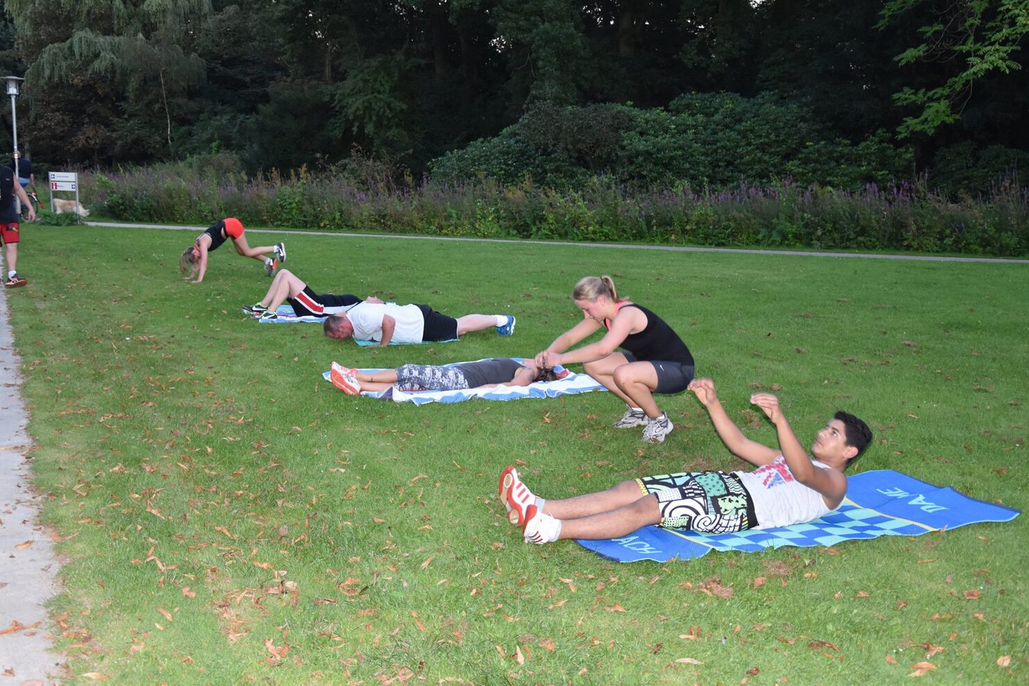 Gruppe von Personen macht Fitness&uuml;bungen auf Handt&uuml;chern im Freien auf einer gr&uuml;nen Wiese.
