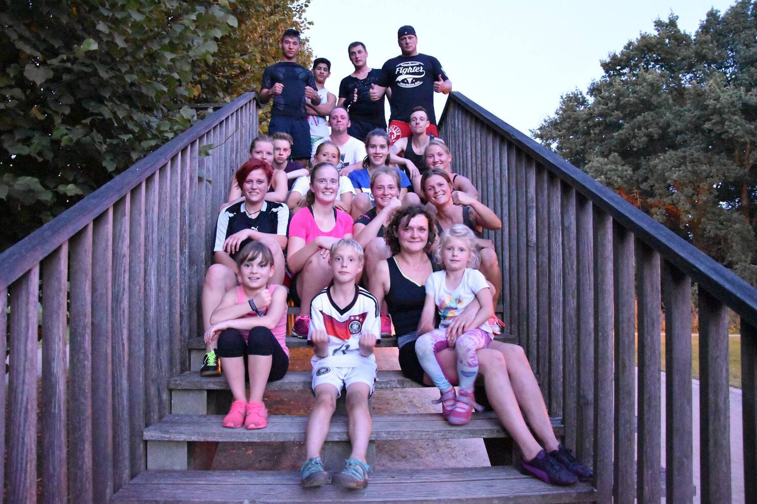 Gruppe von Jugendlichen und Kindern posiert auf einer Treppe unter B&auml;umen bei D&auml;mmerung, l&auml;chelnd in die Kamera.
