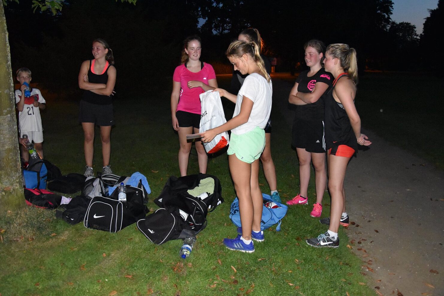 Gruppe von sechs Jugendlichen, die in einem Park stehen und sich &uuml;ber Sportausr&uuml;stung austauschen.