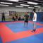 Trainingseinheit in einem Kampfsportstudio mit mehreren Teilnehmern auf einer blauen und roten Matte.