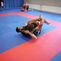 Zwei Sportler praktizieren Grappling auf einer blau-roten Matte in einem Trainingsraum.