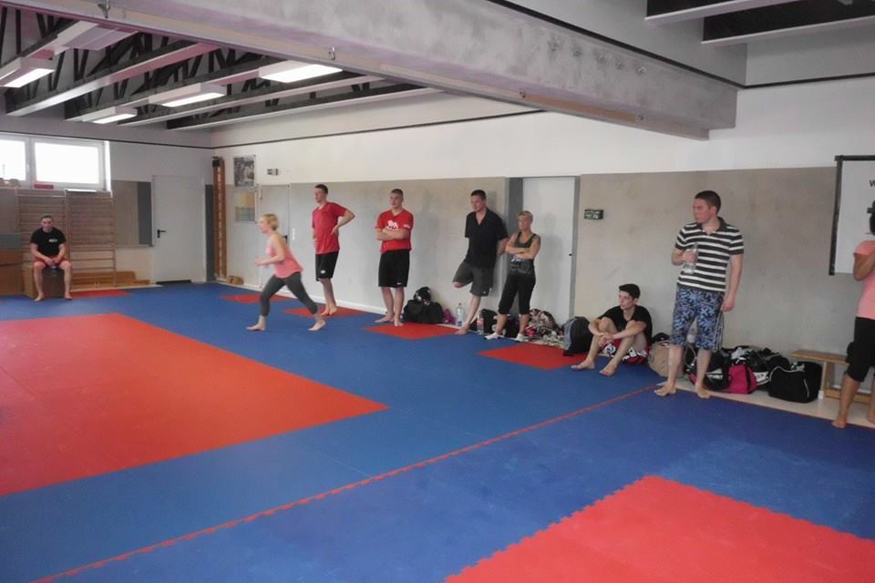 Sporthalle mit blauen und roten Matten; eine Person l&auml;uft, w&auml;hrend andere am Rand zuschauen.