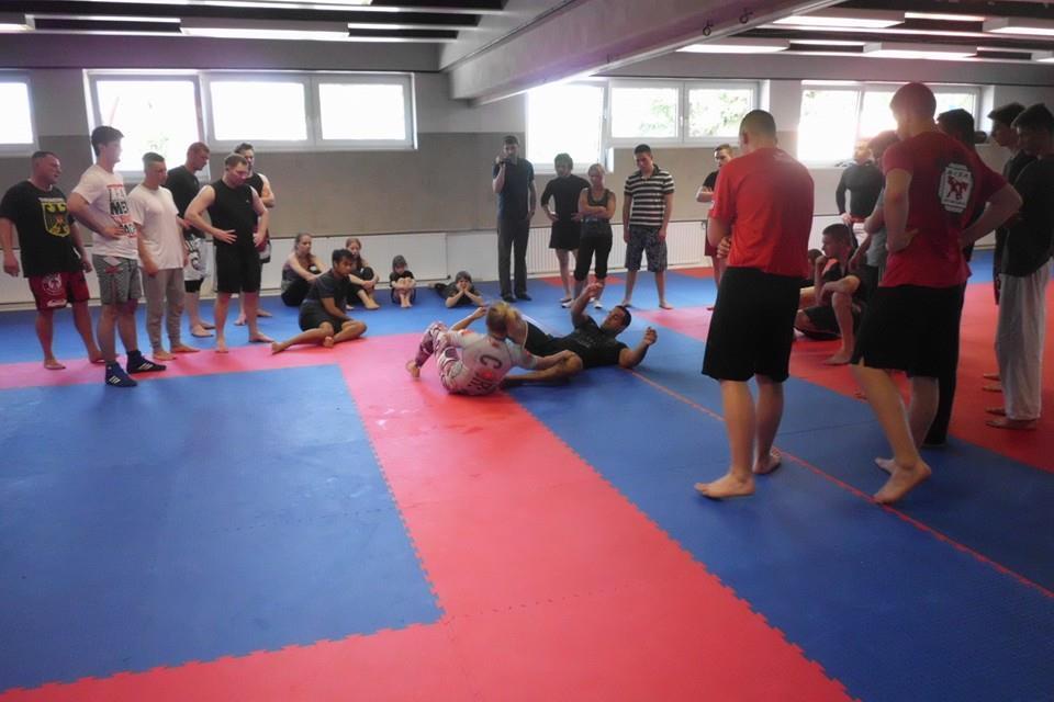 Gruppentraining im Kampfkunstraum mit Teilnehmern, die Techniken auf blauen und roten Matten demonstrieren.