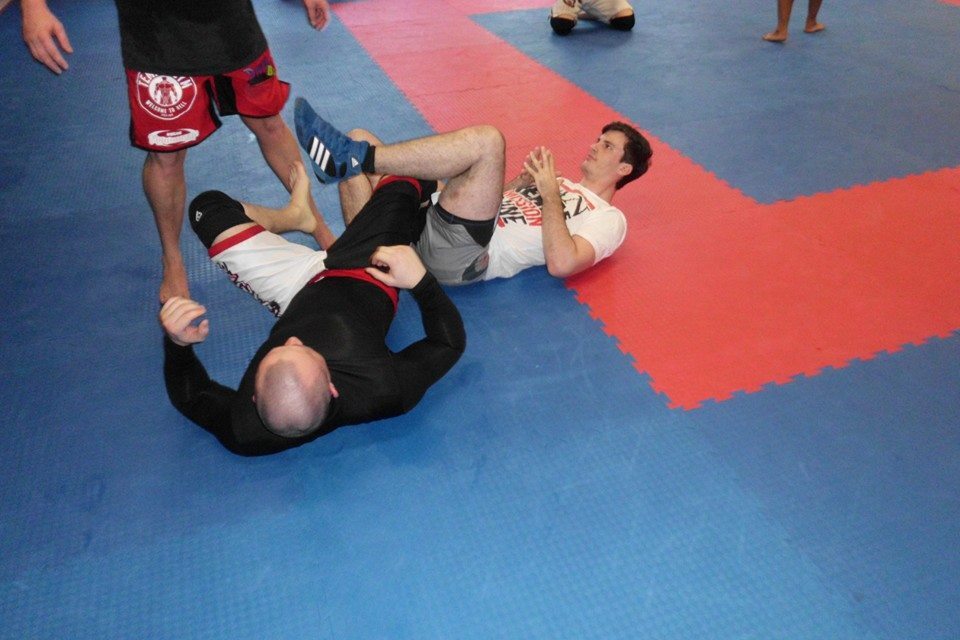 Zwei K&auml;mpfer &uuml;ben auf einer blauen Mattenfl&auml;che. Einer liegt auf dem R&uuml;cken, der andere steht &uuml;ber ihm.