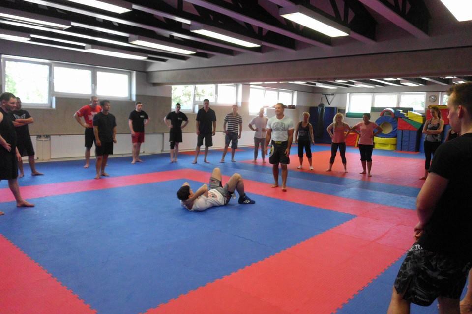 Gruppe von Menschen beobachtet einen Kampfsporttraining, w&auml;hrend ein Teilnehmer am Boden arbeitet.