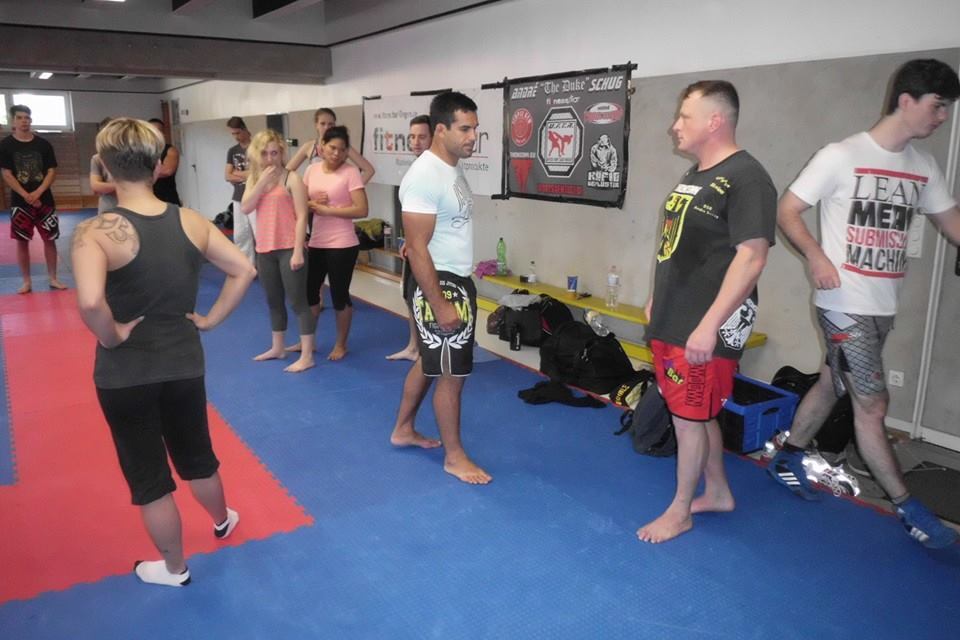 Trainingseinheit in einer Kampfsportschule, Teilnehmer in Sportkleidung stehen auf der Matte und unterhalten sich.