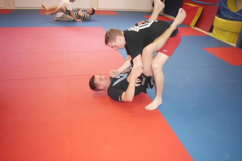 Zwei M&auml;nner &uuml;ben Kampfsport auf einer Matte, einer liegt auf dem R&uuml;cken, der andere ist direkt &uuml;ber ihm positioniert.