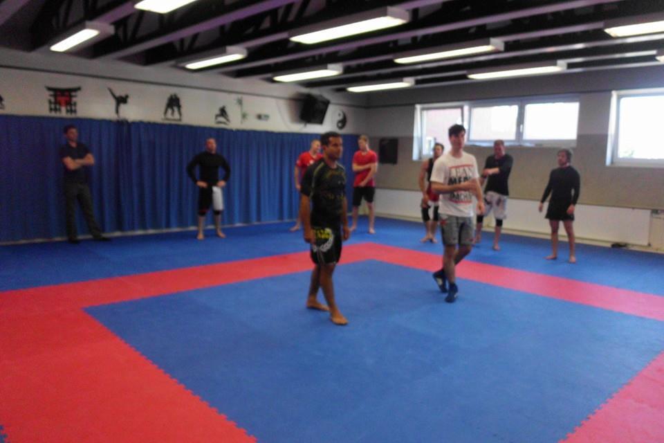Gruppentraining in einem Kampfsportraum mit mehreren Menschen auf einer blauen und roten Matte.