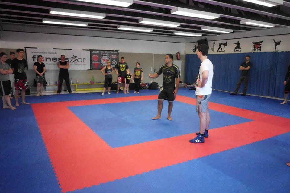 Trainingseinheit in einem Kampfsportstudio mit mehreren Teilnehmern auf einer blauen und roten Matte.